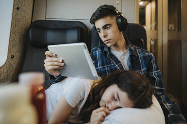 Junge vor Tablet-PC mit Schwester auf dem Schoß im Zug - MASF39974