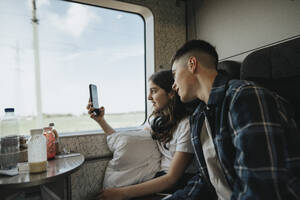 Sister sharing smart phone with brother while doing photography in train - MASF39989