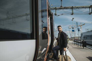 Seitenansicht eines Mannes mit Gepäck beim Einsteigen in einen Zug am Bahnhof - MASF39998