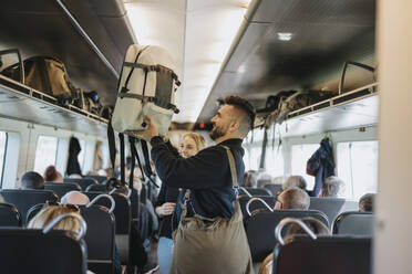 Seitenansicht eines Mannes, der einer Familie hilft, ihr Gepäck auf ein Regal im Zug zu laden - MASF40002