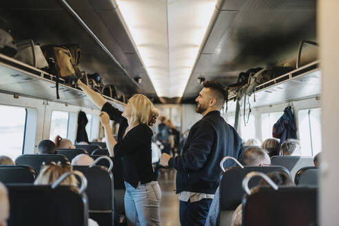 Woman helping man to load luggage on shelf in train - MASF40003