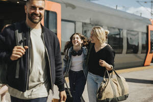 Glückliche Familie beim Aussteigen aus dem Zug am Bahnhof an einem sonnigen Tag - MASF40005