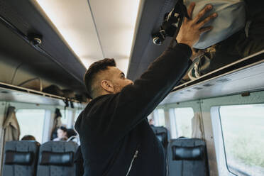 Seitenansicht eines Mannes, der im Zug Gepäck auf ein Regal lädt - MASF40006