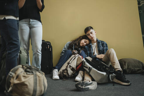 Bruder und Schwester ruhen sich aus, während sie inmitten von Gepäck in der Nähe der gelben Wand sitzen - MASF40017