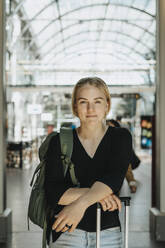 Porträt einer lächelnden Frau mit Gepäck auf einem Bahnhof - MASF40018