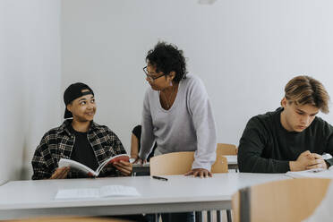 Lehrer schaut auf einen lächelnden männlichen Schüler, der im Klassenzimmer sitzt - MASF40041