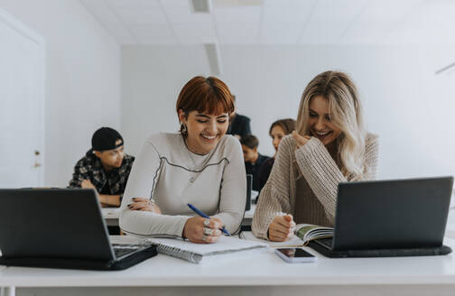 Fröhliche Studentinnen lernen gemeinsam am Schreibtisch im Klassenzimmer - MASF40046