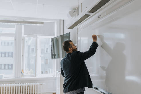 Side view of mature male professor writing on whiteboard in classroom - MASF40054