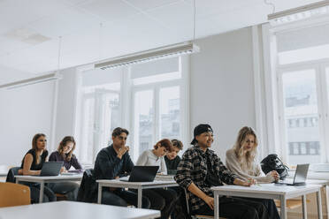 Multiracial male and female students sitting at desk in classroom - MASF40056