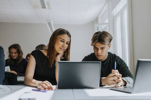 Multiracial male and female students sharing laptop at desk in classroom - MASF40061