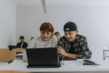 Ein Mann und eine Frau benutzen gemeinsam einen Laptop am Schreibtisch im Klassenzimmer - MASF40065