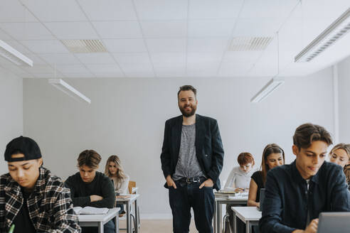 Porträt eines lächelnden Professors, der mit den Händen in den Taschen inmitten von Studenten steht - MASF40069