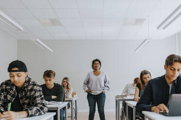 Porträt einer Lehrerin mit Händen in den Taschen, die inmitten von Schülern steht - MASF40070