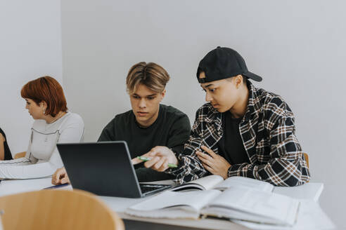 Männliche Schüler benutzen gemeinsam einen Laptop am Schreibtisch im Klassenzimmer - MASF40074