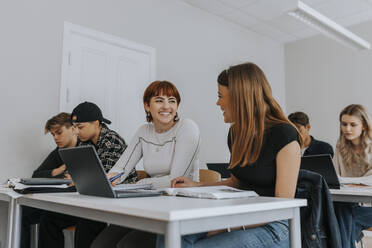 Lächelnde Teenager-Mädchen, die mit Freunden am Schreibtisch sitzen und gemeinsam im Klassenzimmer lernen - MASF40075