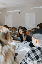 Smiling teenage girl sitting with friends while studying in classroom - MASF40077