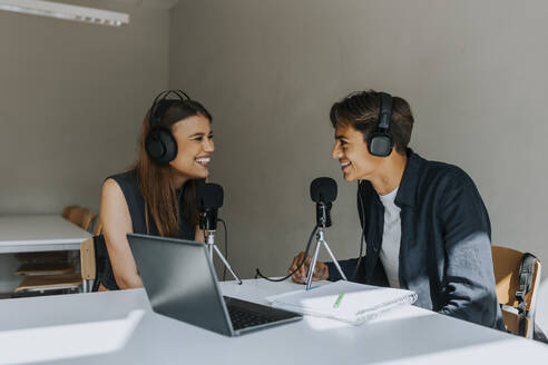 Glückliche männliche und weibliche Schüler, die sich beim Podcasting im Klassenzimmer anschauen - MASF40086