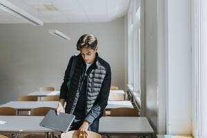 Jugendlicher mit Laptop im Klassenzimmer stehend - MASF40095