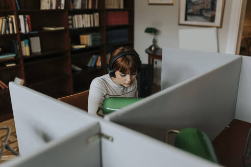 Teenage girl wearing wireless headphones while sitting in library - MASF40098