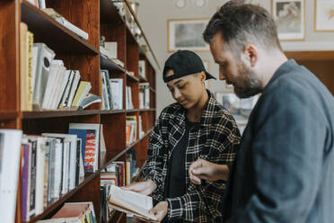 Junger Mann diskutiert mit Professor in der Bibliothek über ein Buch - MASF40106