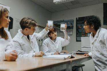 Lehrer und Schüler untersuchen eine Chemikalie in einem Becherglas im Schullabor - MASF40109