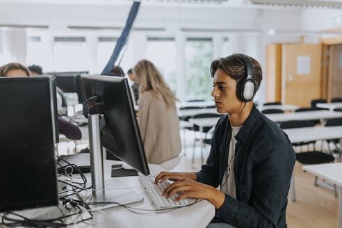 Jugendlicher hört über Kopfhörer zu, während er einen Computer im Schullabor benutzt - MASF40113