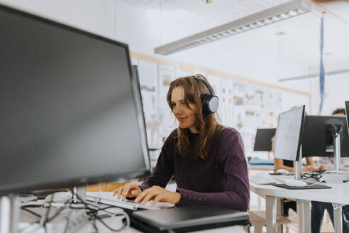 Young woman listening through headphones while using computer in school lab - MASF40114