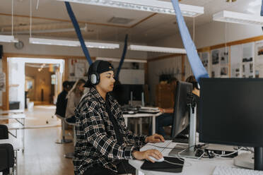 Junger Mann, der einen Computer benutzt und über Kopfhörer in einem Labor lauscht - MASF40115