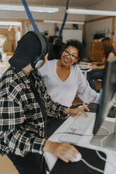 Smiling teacher looking at young male student in computer lab - MASF40116