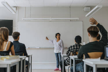 Reife weibliche Lehrerin, die auf eine Tafel zeigt, während sie Schüler im Klassenzimmer unterrichtet - MASF40146