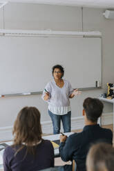 Teacher gesturing while teaching students sitting in classroom - MASF40147
