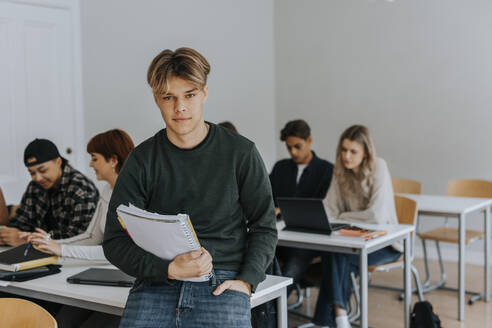 Porträt eines Teenagers mit einem Buch, das auf einem Schreibtisch im Klassenzimmer liegt - MASF40151