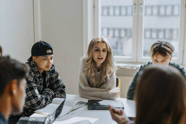 Junge Studentin sitzt mit Freunden am Schreibtisch im Klassenzimmer - MASF40159