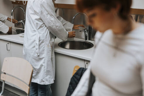 Mittelteil einer jungen Studentin beim Waschen eines Bechers im Waschbecken eines wissenschaftlichen Labors - MASF40168