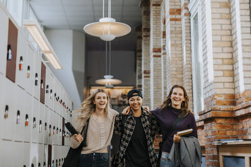 Happy young male and female students walking with arms around in corridor - MASF40173