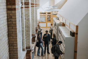 Blick von oben auf männliche und weibliche Studenten an einem Spind im Korridor - MASF40179