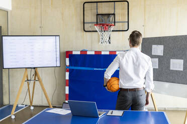 Businessman standing with basketball in front of hoop and device screen - PESF04041