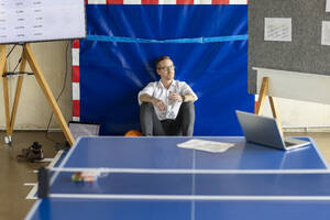 Nachdenklicher Geschäftsmann sitzt hinter einem Tennistisch im Büro - PESF04048