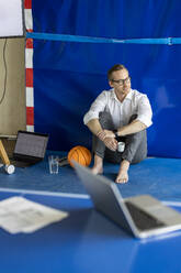 Contemplative businessman sitting behind tennis table in office - PESF04049