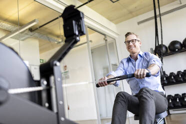 Lächelnder Geschäftsmann beim Training mit Geräten im Büro-Fitnessstudio - PESF04092