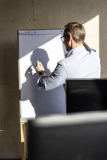 Businessman writing on flipchart in office - PESF04098