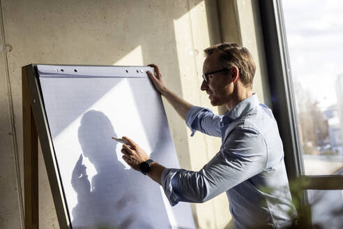 Lächelnder Geschäftsmann schreibt auf Flipchart - PESF04099