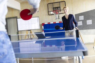 Lächelnde Geschäftsfrau spielt Tennis mit einem Kollegen in einem modernen Büro - PESF04130