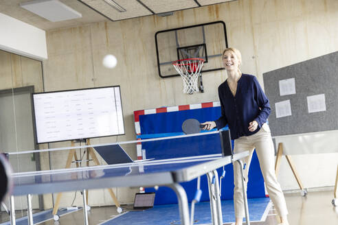 Glückliche reife Geschäftsfrau spielt Tennis im Büro - PESF04131