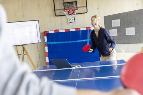 Happy businesswoman playing tennis in modern office - PESF04132