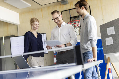 Smiling businessman reading document with colleagues in modern office - PESF04135