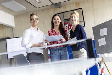 Glückliche Geschäftsleute stehen mit Dokumenten in einem modernen Büro - PESF04144