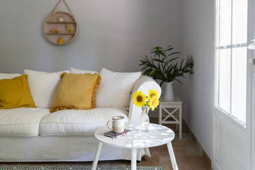 Wohnzimmer mit weißem Sofa, Sonnenblumen und Tasse auf dem Tisch zu Hause - SVKF01656
