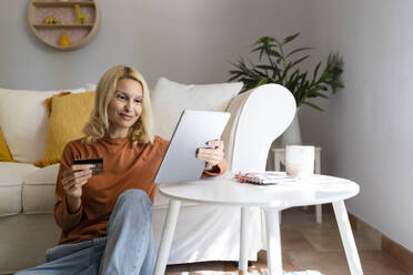 Blonde Frau mit Kreditkarte beim Online-Shopping über einen Tablet-PC zu Hause - SVKF01665
