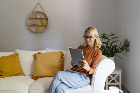 Lächelnde reife Frau mit Brille, die einen Tablet-PC im Wohnzimmer zu Hause benutzt - SVKF01667